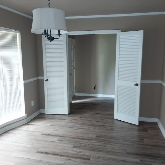 unfurnished dining area with baseboards, crown molding, wood finished floors, and a chandelier