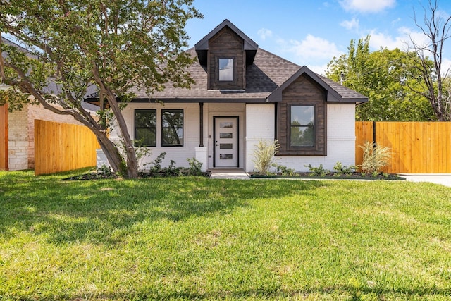 view of front of property with a front lawn, brick siding, fence, and a shingled roof