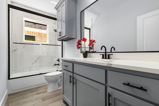 full bath with wood tiled floor, enclosed tub / shower combo, toilet, vanity, and baseboards