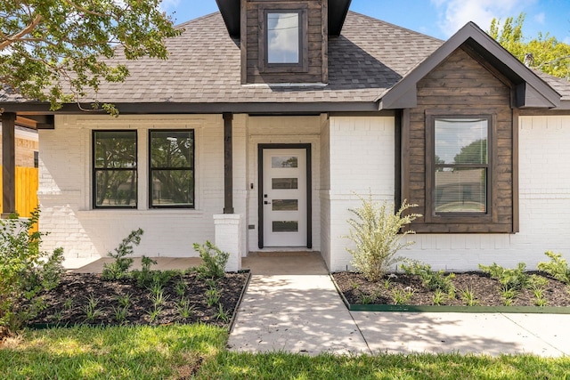 view of exterior entry featuring brick siding, roof with shingles, and a porch