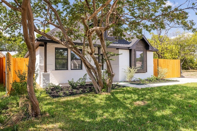 view of front of property with fence, a shingled roof, brick siding, and a front yard