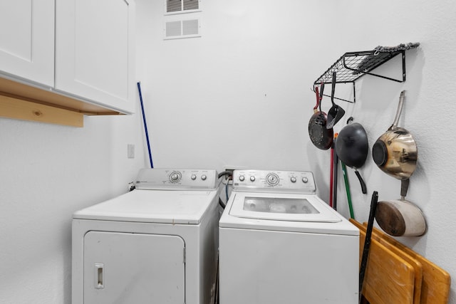 clothes washing area featuring washing machine and dryer, visible vents, and cabinet space