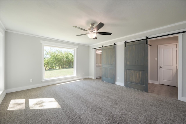 unfurnished bedroom with ceiling fan, a barn door, carpet, baseboards, and ornamental molding