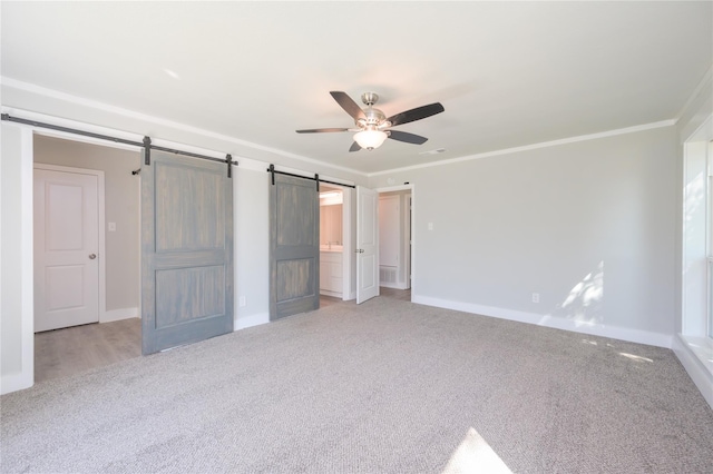 unfurnished bedroom featuring baseboards, a barn door, carpet, and ornamental molding