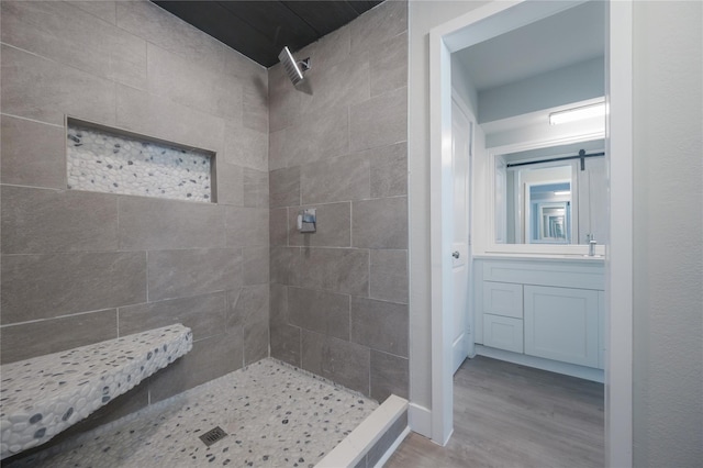 full bath featuring vanity, wood finished floors, and tiled shower