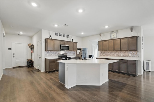 kitchen featuring a sink, stainless steel appliances, decorative backsplash, light countertops, and an island with sink