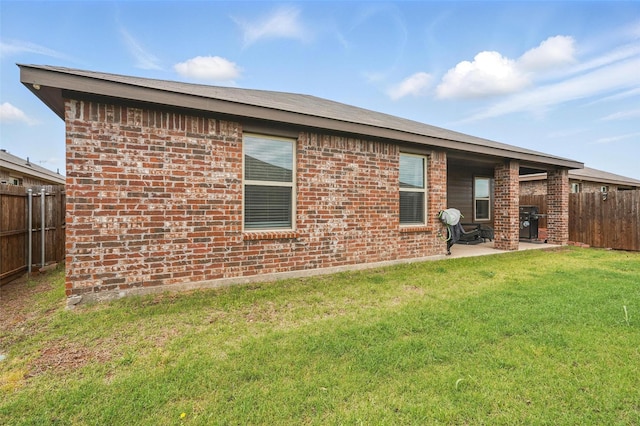 back of house featuring a patio, brick siding, fence private yard, and a lawn