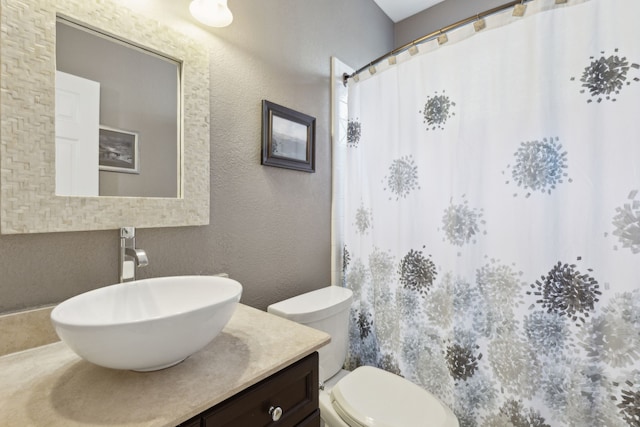 bathroom featuring toilet, a textured wall, vanity, and curtained shower