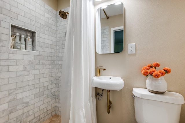 bathroom featuring a tile shower, toilet, and a sink