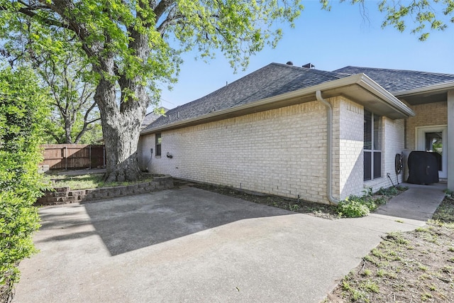 1220 Chaparral Ln, Granbury, TX 76048 - view of home's exterior featuring brick siding, a shingled roof, a patio, and fence