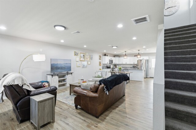 living room featuring stairway, visible vents, and light wood-type flooring