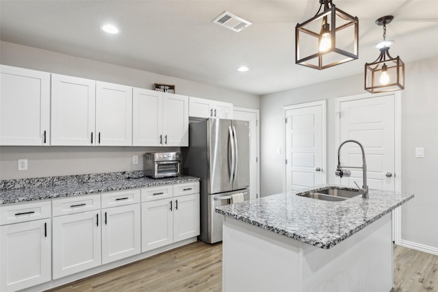 kitchen featuring a sink, light wood finished floors, white cabinetry, visible vents, and freestanding refrigerator
