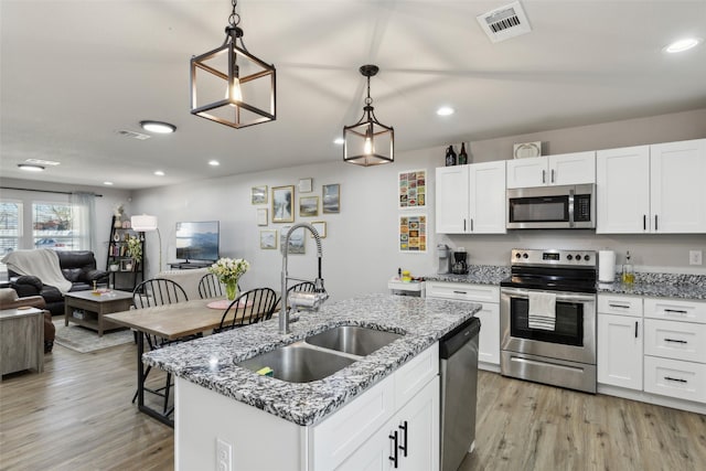 kitchen with a sink, open floor plan, light wood finished floors, appliances with stainless steel finishes, and visible vents