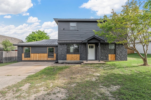 back of property with fence, concrete driveway, stone siding, a lawn, and metal roof
