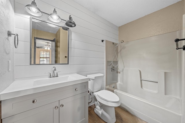 bathroom with toilet, shower / bathing tub combination, wood finished floors, wood walls, and vanity