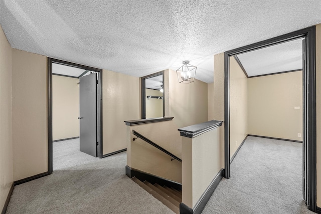 hallway featuring baseboards, a textured ceiling, an upstairs landing, and light colored carpet