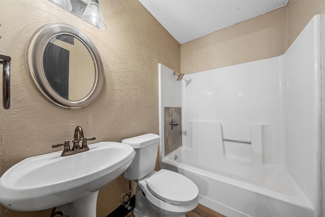 bathroom featuring a sink, a textured ceiling, washtub / shower combination, a textured wall, and toilet