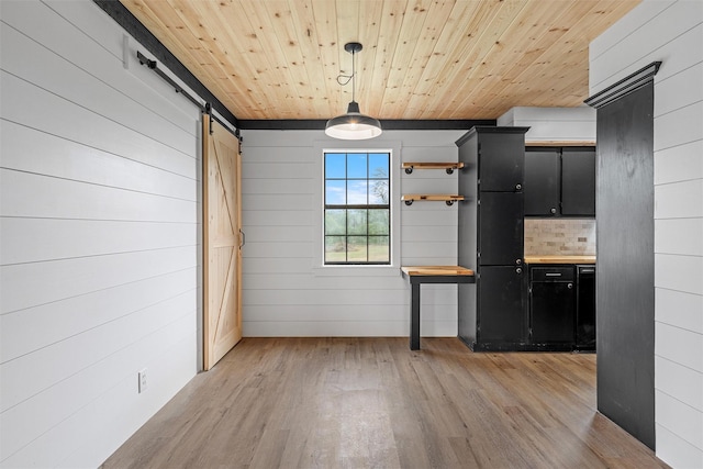 unfurnished dining area with a barn door, wooden walls, light wood-type flooring, and wooden ceiling