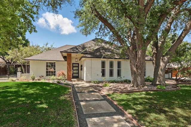 single story home featuring fence, a front lawn, brick siding, and roof with shingles