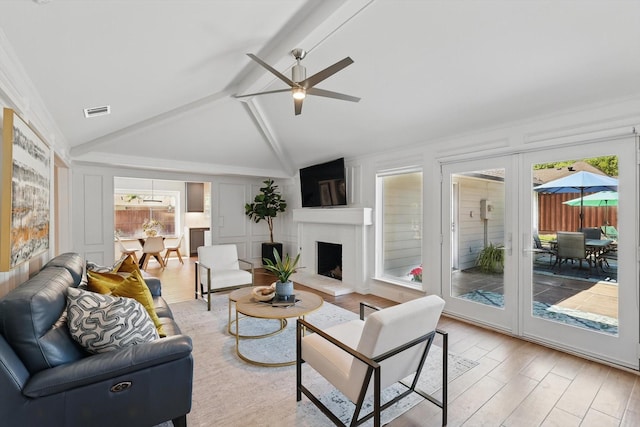 living area featuring a decorative wall, vaulted ceiling with beams, light wood-type flooring, ceiling fan, and visible vents
