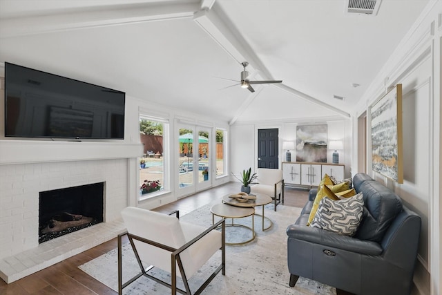 living room featuring wood finished floors, lofted ceiling with beams, ceiling fan, a brick fireplace, and visible vents