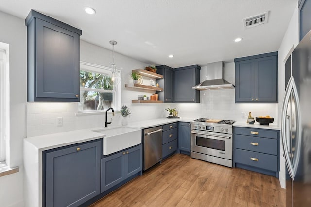 kitchen featuring visible vents, a sink, wall chimney exhaust hood, tasteful backsplash, and appliances with stainless steel finishes