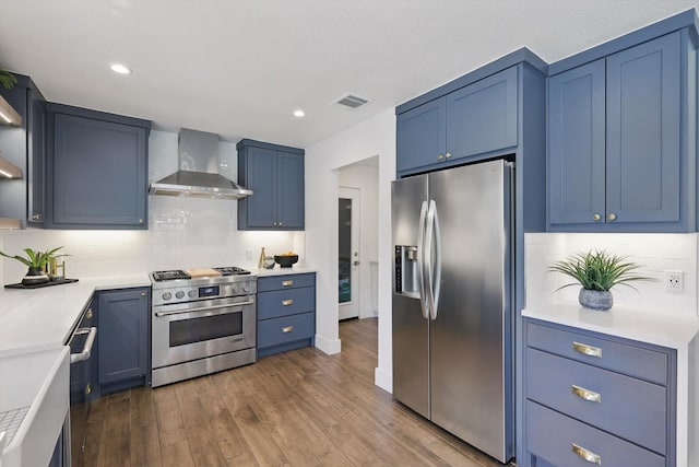 kitchen featuring stainless steel appliances, light countertops, dark wood finished floors, wall chimney exhaust hood, and visible vents