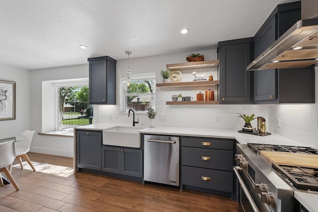 kitchen with a sink, backsplash, wall chimney range hood, light countertops, and appliances with stainless steel finishes