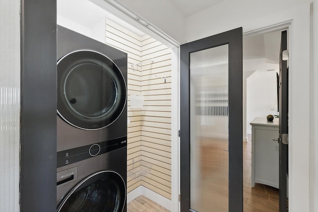 laundry room with stacked washer / dryer, wood finished floors, and laundry area