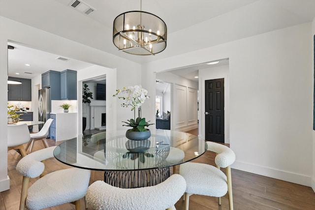 dining room featuring wood finished floors, visible vents, baseboards, and a notable chandelier