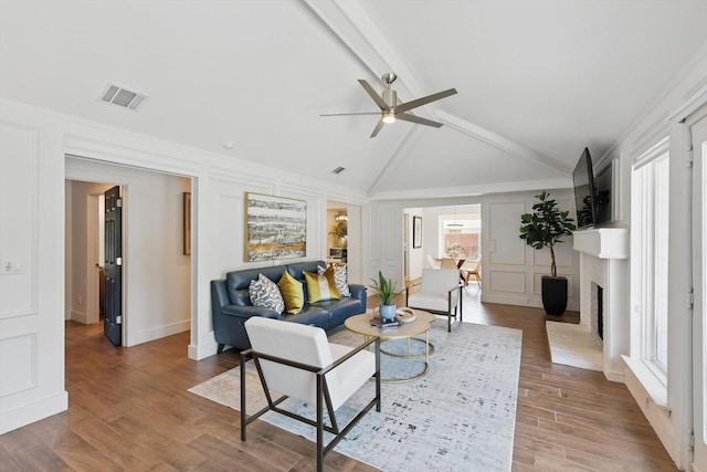 living area featuring lofted ceiling with beams, visible vents, a ceiling fan, wood finished floors, and a decorative wall