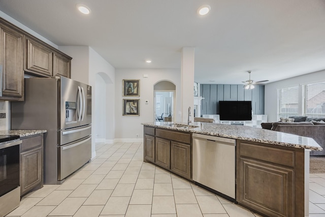 kitchen with open floor plan, ceiling fan, arched walkways, a sink, and appliances with stainless steel finishes