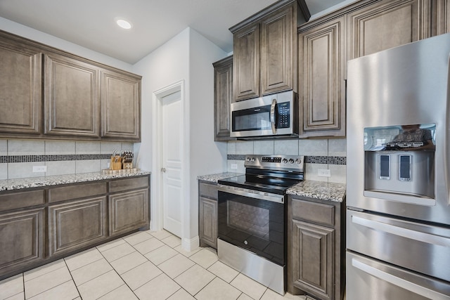 kitchen featuring decorative backsplash, dark brown cabinetry, light stone countertops, stainless steel appliances, and light tile patterned flooring