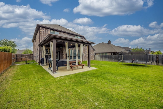 back of house with brick siding, a fenced backyard, a trampoline, and a patio area