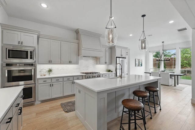 kitchen featuring appliances with stainless steel finishes, a sink, light countertops, premium range hood, and visible vents