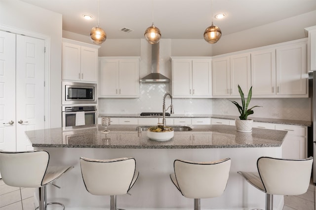 kitchen featuring white cabinets, a sink, visible vents, wall chimney range hood, and appliances with stainless steel finishes