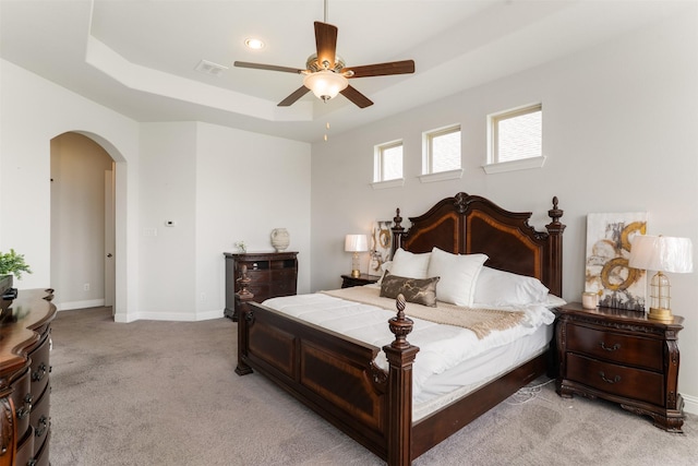bedroom featuring light carpet, arched walkways, baseboards, visible vents, and a raised ceiling