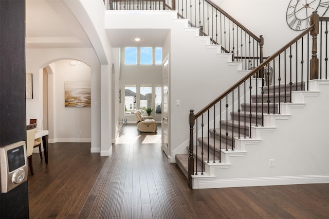 entryway with wood finished floors, stairs, a towering ceiling, and baseboards