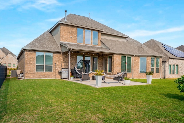 rear view of house featuring brick siding, a patio area, a lawn, fence private yard, and roof with shingles