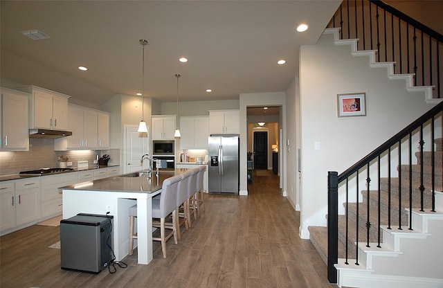 kitchen featuring a sink, decorative backsplash, stainless steel appliances, under cabinet range hood, and wood finished floors