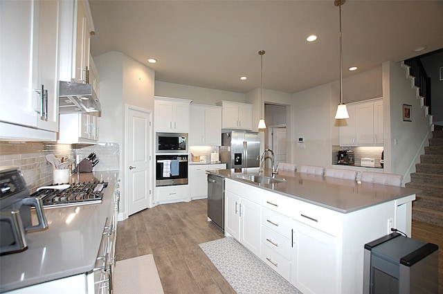 kitchen with white cabinetry, a sink, stainless steel appliances, under cabinet range hood, and wood finished floors