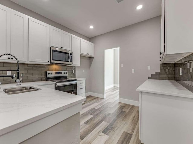kitchen with a sink, backsplash, white cabinets, baseboards, and appliances with stainless steel finishes