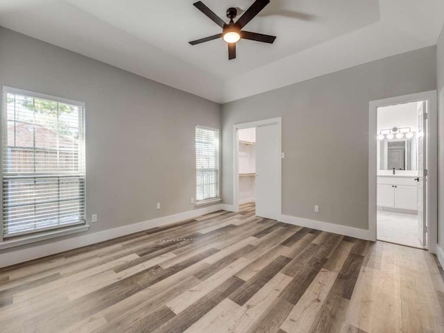 unfurnished bedroom featuring baseboards, wood finished floors, ceiling fan, connected bathroom, and a walk in closet