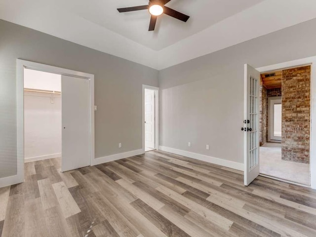 unfurnished bedroom featuring light wood-type flooring, a spacious closet, baseboards, and french doors