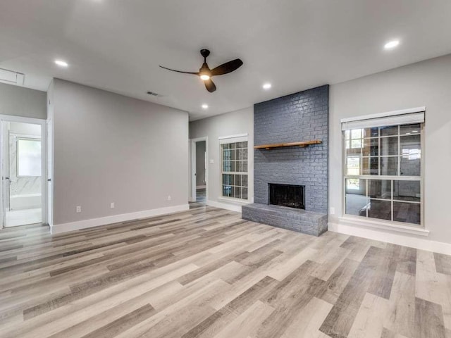 unfurnished living room with a fireplace, light wood-style floors, a wealth of natural light, and a ceiling fan