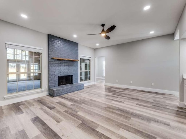 unfurnished living room featuring baseboards, a ceiling fan, light wood-style floors, and a fireplace