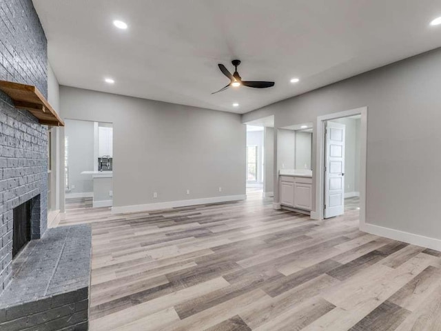 unfurnished living room featuring baseboards, a ceiling fan, light wood-style floors, and a fireplace