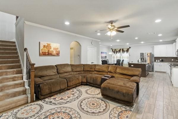 living room with a ceiling fan, recessed lighting, stairs, crown molding, and arched walkways