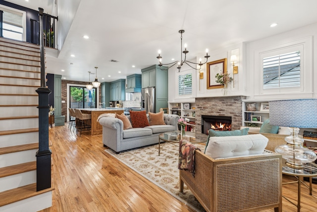 living room featuring a notable chandelier, a brick fireplace, stairs, and light wood-type flooring