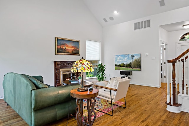 living area featuring visible vents, a premium fireplace, wood finished floors, stairs, and high vaulted ceiling